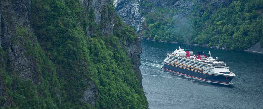 Um navio de cruzeiro Disney navegando entre 2 grandes montanhas