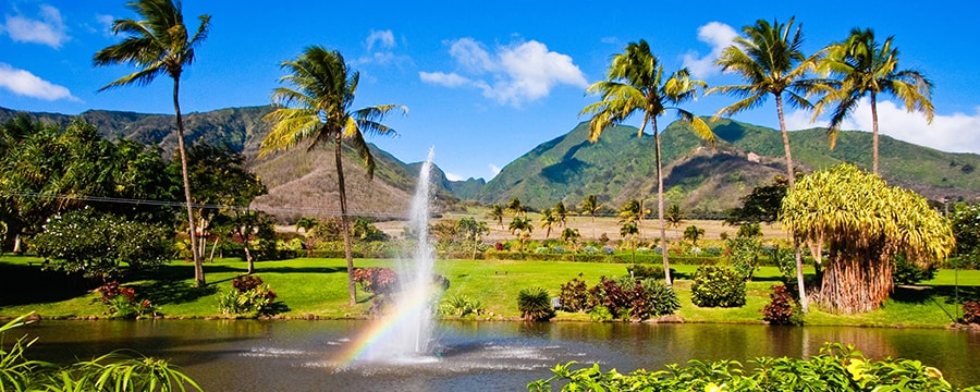 A fountain sprays upward from a pond, creating a rainbow near a replica of a Polynesian village A fountain sprays upward from a pond, creating a rainbow near a replica of a Polynesian village