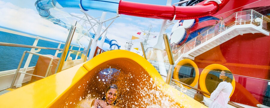 A smiling young woman watersliding with arms across her chest and feet first into the Splash Zone