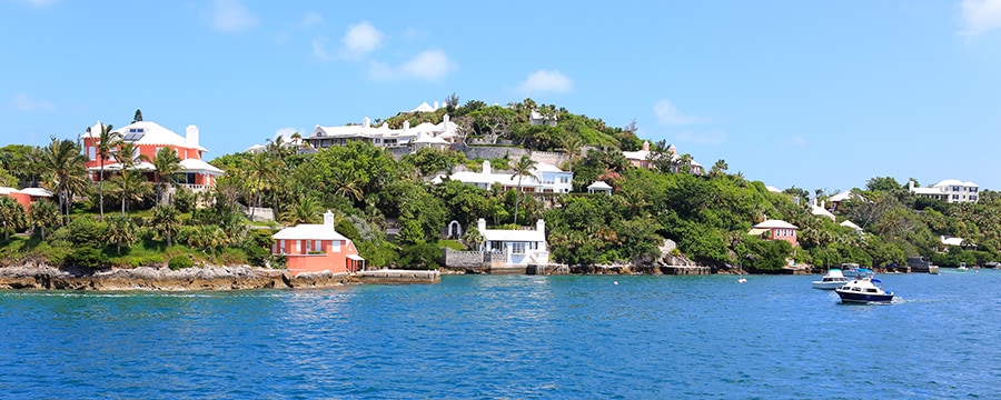 A shoreline pressed up against a grassy hill with buildings and trees A shoreline pressed up against a grassy hill with buildings and trees