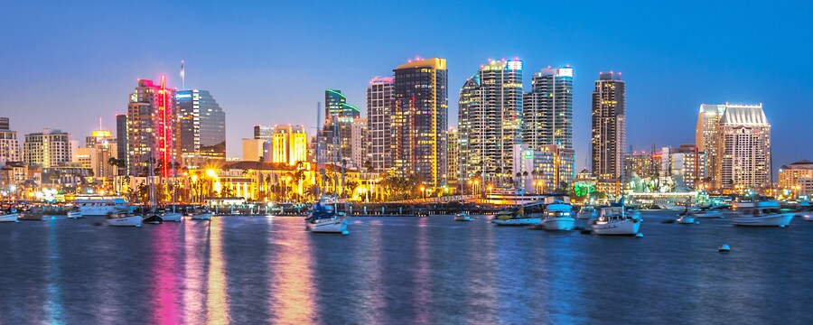 City skyscrapers are outlined by bright neon lights that reflect on the ocean