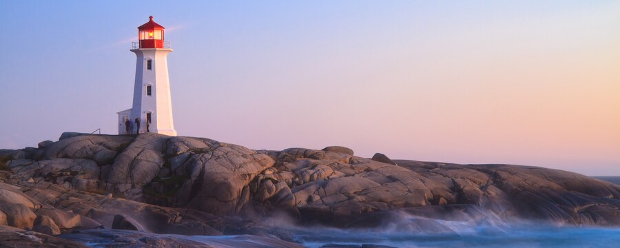 Un faro se alza sobre rocas suaves y las olas del océano al atardecer Un faro se alza sobre rocas suaves y las olas del océano al atardecer