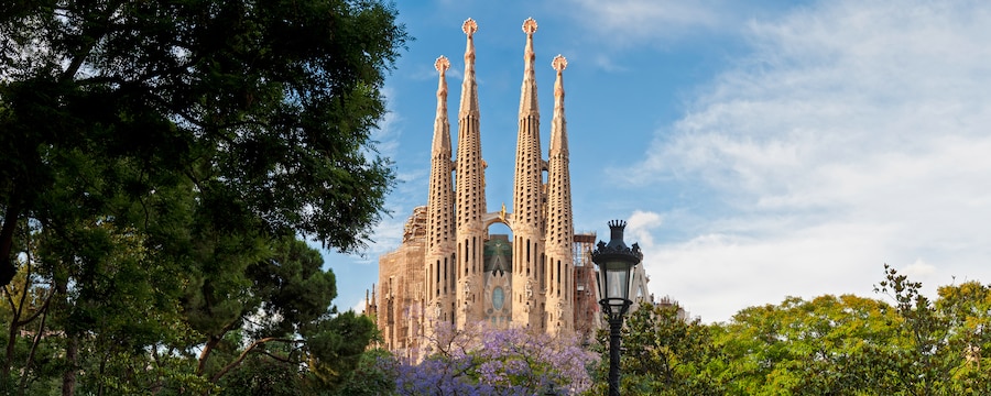 A tall European castle with 4 pointed towers is surrounded by flowering trees A tall European castle with 4 pointed towers is surrounded by flowering trees