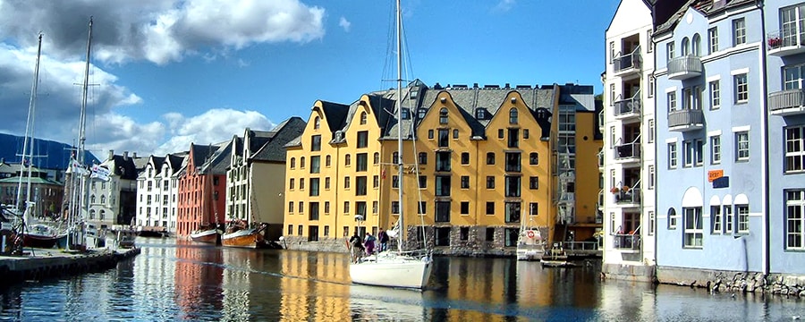 Identical 6-story houses and a marina line the waterways of a canal while a sailboat coasts between them Identical 6-story houses and a marina line the waterways of a canal while a sailboat coasts between them