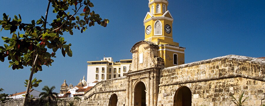 A wall built of stone with three gateways separates a plaza from a town with modern and colonial buildings