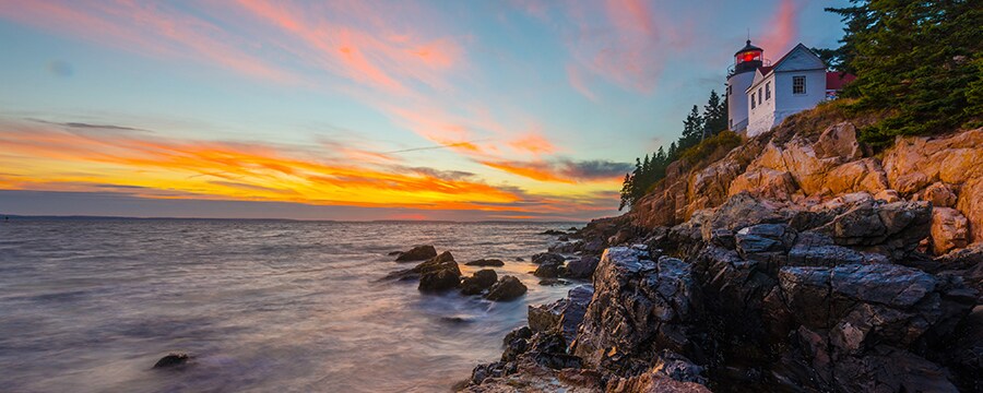 A lighthouse by the ocean on the edge of a rocky cliff featuring trees
