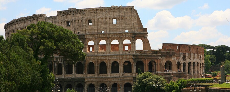 The ancient roman Colosseum stands tall on a sunny day above crowds of onlookers
