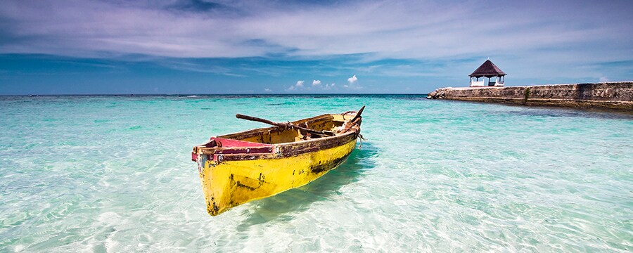 An old rowboat floats in clear waters next to a breaker with a small gazebo structure