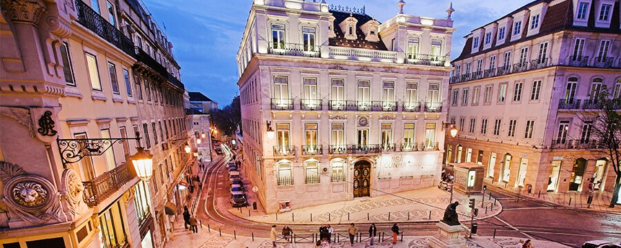Baroque style buildings, amid busy streets with people and cars at night