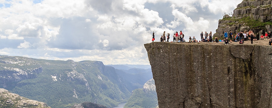 An assortment of people sitting and standing above a sheer cliff overlooking a valley An assortment of people sitting and standing above a sheer cliff overlooking a valley