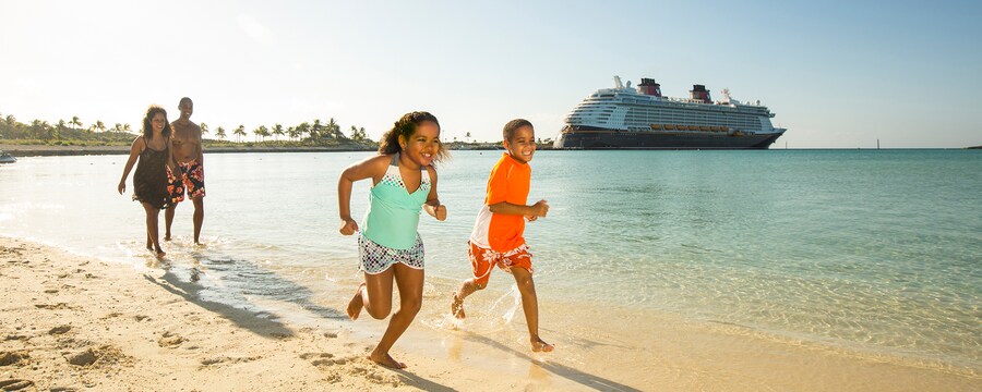 A family walks along a stretch of beach near a Disney Cruise Line ship