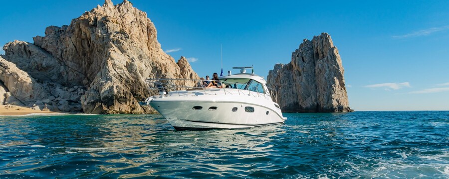 A yacht sailing on the ocean alongside a sandy beach and large rock formations