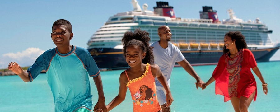 Una familia joven y feliz de 4 miembros tomados de la mano en una playa junto a un crucero de Disney Una familia joven y feliz de 4 miembros tomados de la mano en una playa junto a un crucero de Disney