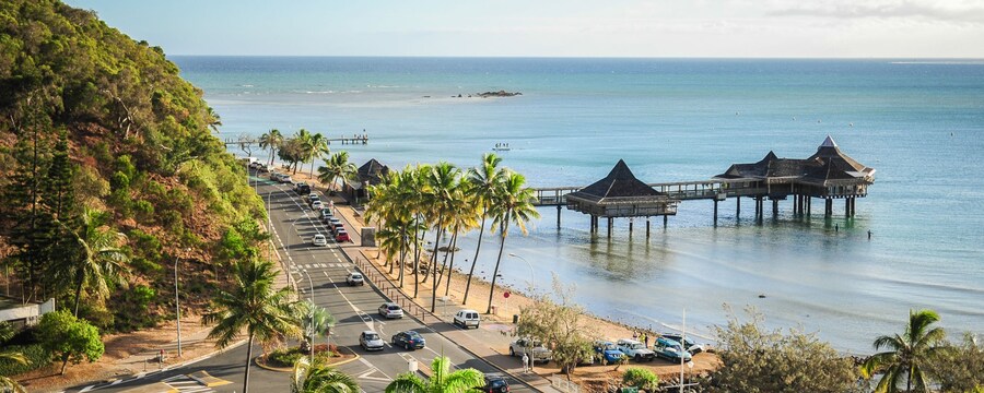 Un entorno tropical con un camino costero, un muelle y cabañas sobre el agua
