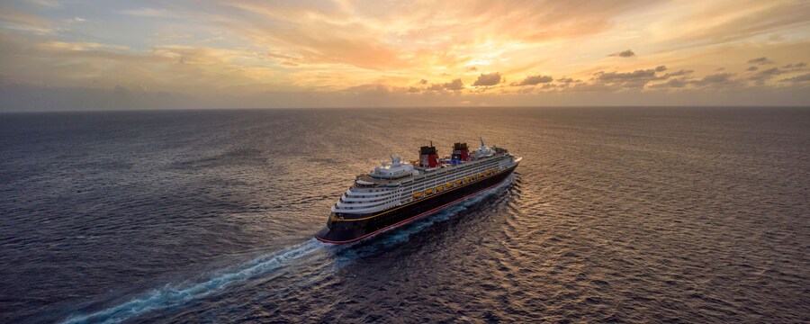 A Disney Cruise Line ship sails along in tranquil, open water, with a beautiful sunset in the background