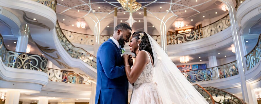 Una novia y un novio sonriendo tomados de las manos en el Grand Hall en Disney Wish