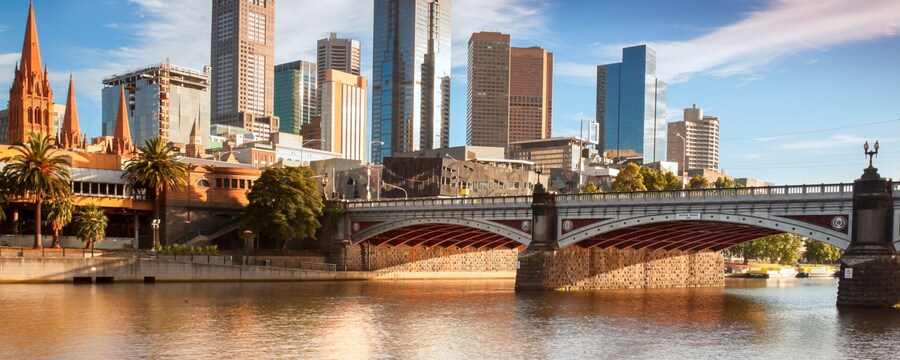 El paisaje urbano de Melbourne revela una iglesia clásica y rascacielos junto a un río y puente
