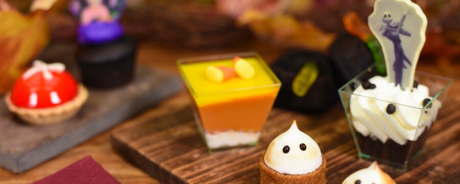 Several wooden slates holding small Halloween theme desserts on a spoon resting on a napkin