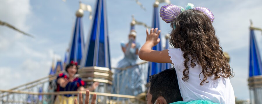 Little girl sits on her father's shoulder's as she waves to Snow White passing by on a float