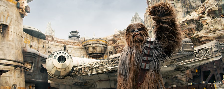 Chewbacca raises a fist in triumph in front of the Millennium Falcon at Star Wars: Galaxy’s Edge