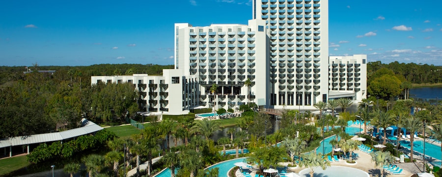 A large hotel featuring a winding pool lined with reclining beach chairs and palm trees