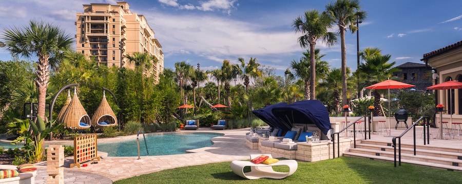 A resort pool area features abstract furniture and umbrellas, as well as giant Jenga and Connect 4 games