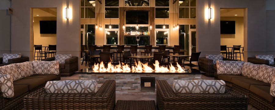 Rattan sectional sofas around a large firepit, with a bar in the background