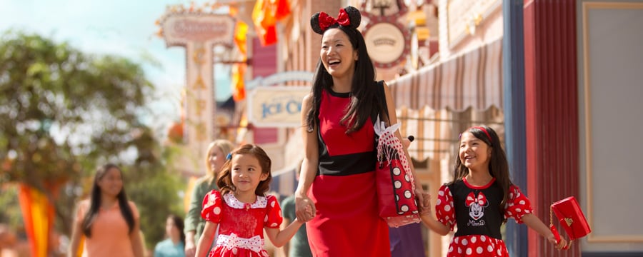 Una madre con Orejas de Minnie lleva de la mano a sus 2 hijas mientras pasean por Main Street U.S.A.