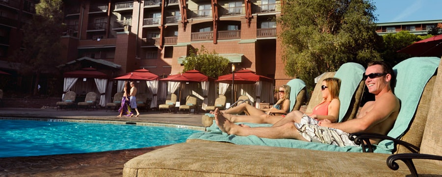 Three Guests in bathing suits sit poolside in lounge chairs at Disney's Grand Californian Hotel & Spa