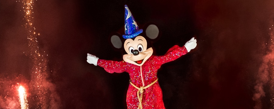 Sorcerer Mickey smiling while sparks fly through the evening sky during a performance of Fantasmic!
