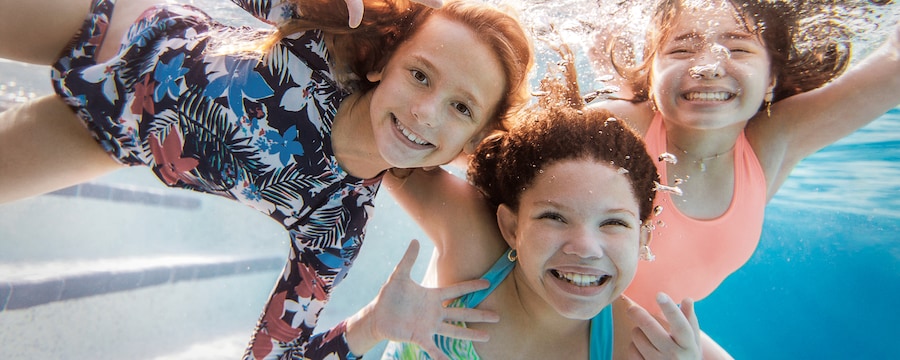 Three girls smiling underwater while swimming in a pool at a Walt Disney World Good Neighbor Hotel