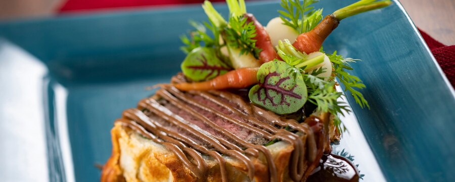 A serving of beef Wellington, garnished with baby carrots, onions and micro greens
