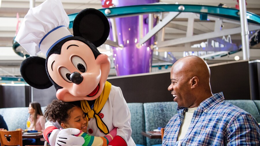 Daughter hugging Mickey Mouse and dining with father at Chef Mickey's