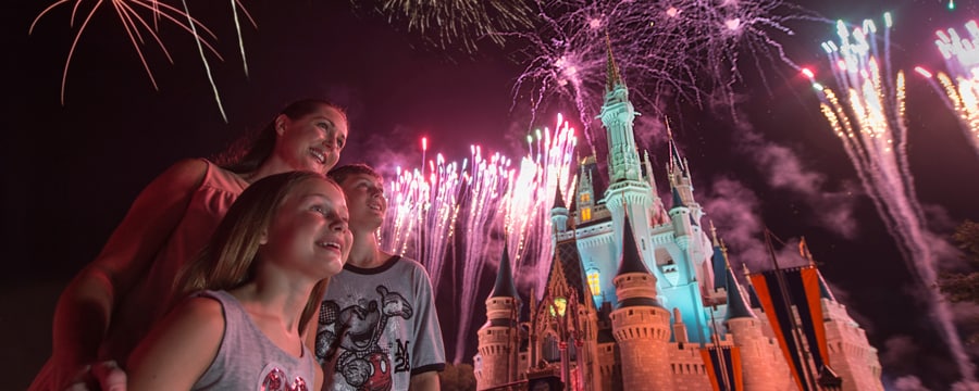 A mother and two children watches in wonder as fireworks burst over Sleeping Beauty Castle illuminating the night sky with color.