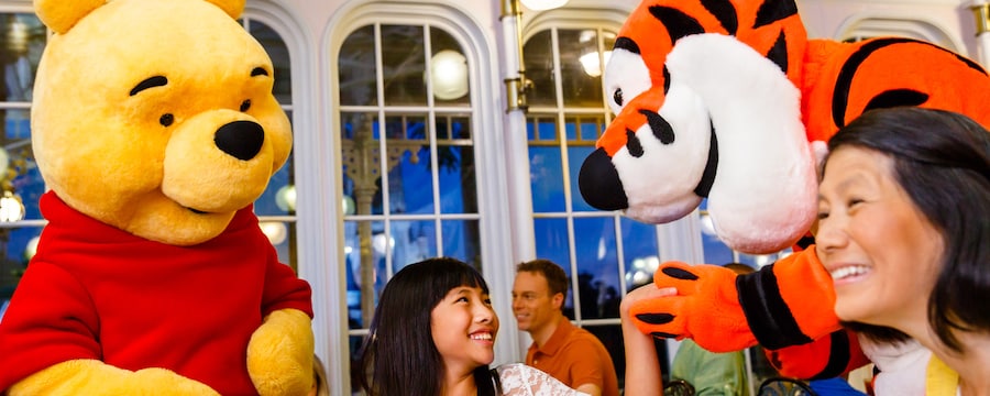 A child smiles as Tigger takes her hand and Winnie the Pooh stands near her