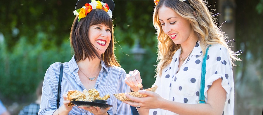 Deux jeunes femmes portant des oreilles de Mickey aux accents floraux profitent d'un repas de service rapide sur le pouce à Epcot