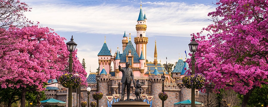 A statue of Walt Disney and Mickey Mouse in front of Sleeping Beauty Castle