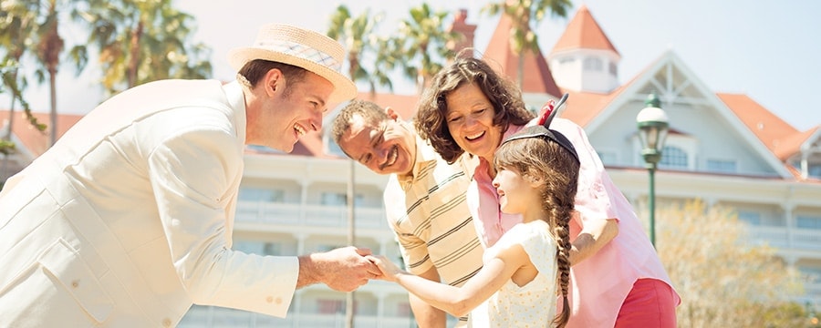 A man wearing a straw hat greets a little girl and her parents outside a hotel
