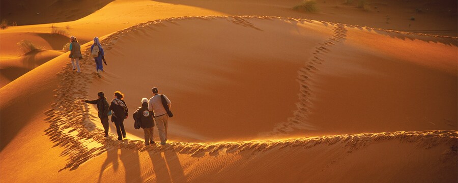 People walk over the sand dunes of the Sahara desert.