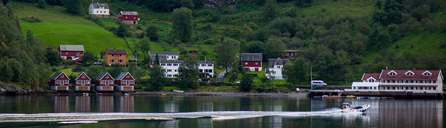 A motorboat passes a lakeside village with houses extending up the mountainside
