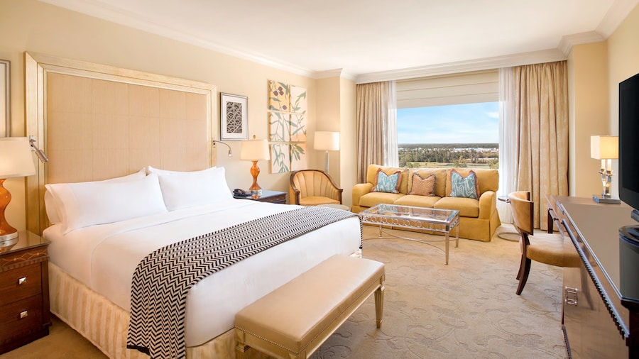 A hotel room with a king bed, a sofa and a view of a golf course