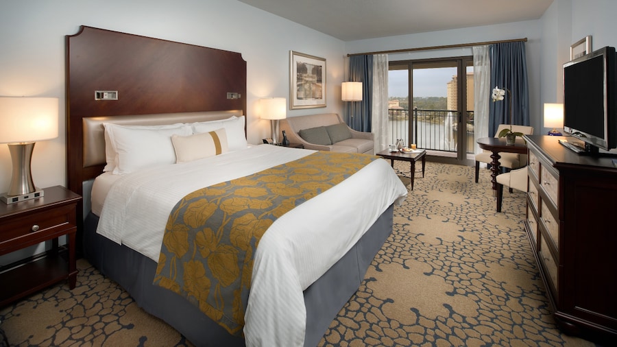 Una habitación de hotel con una cama King Size, una cómoda, sillas, una mesa, un sofá de dos plazas y un balcón