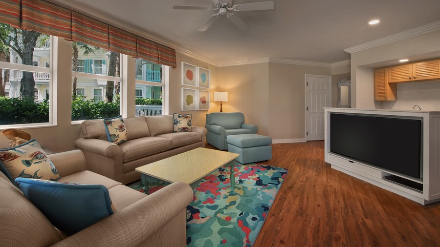 An open kitchen and living area with large view windows, a TV, upholstered chair and ottoman, sofa, love seat, coffee table and lamp