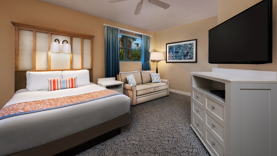 A room with a bed, a nightstand, a couch, a TV, a painting and a lamp