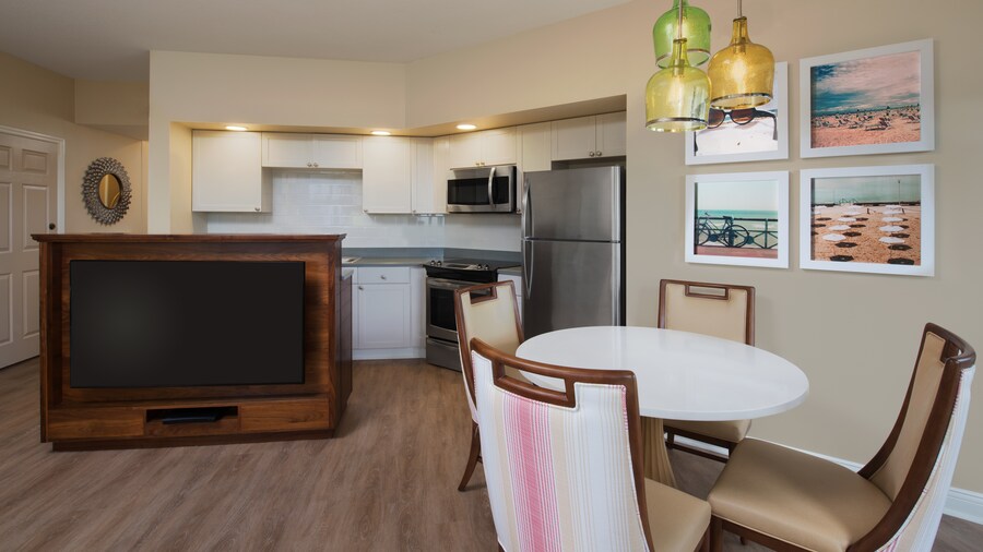 A room with 4 chairs, a table, a TV paintings, a refrigerator, a stove and a microwave