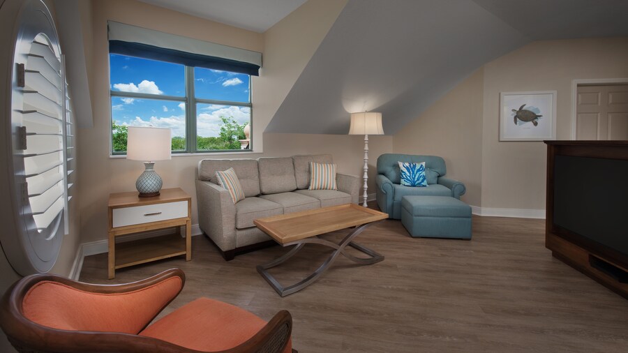A room with a couch, 2 chairs, a TV, an ottoman, paintings, a coffee table and 2 lamps