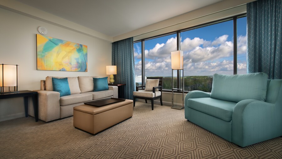 A living area with a couch, an ottoman, a chair, a painting, a loveseat and a window overlooking a lake