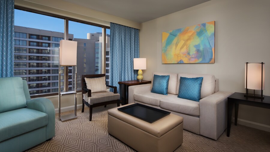 A couch, pillows, a lamp, a painting, a chair, a loveseat and an ottoman near curtains and a window