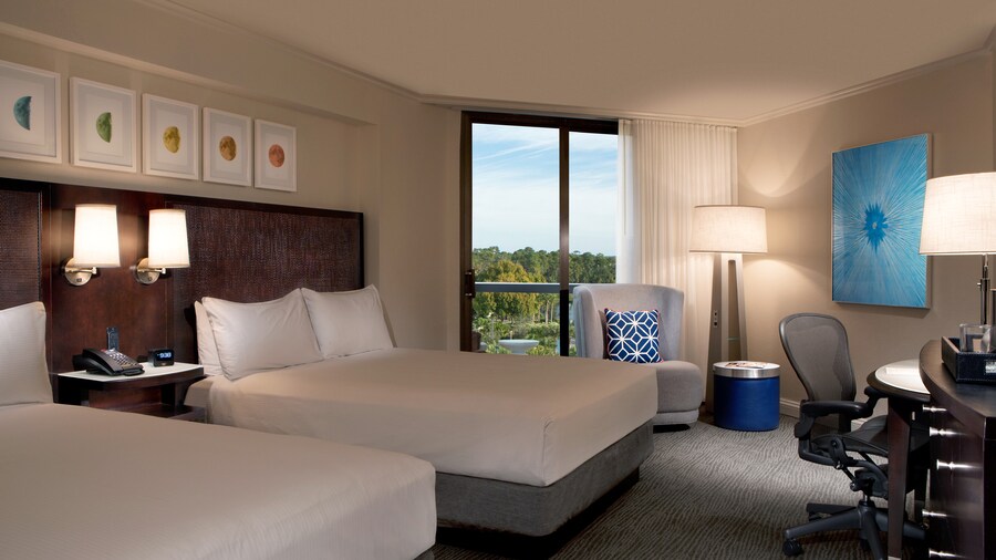 A room with 2 beds, a phone, 2 chairs, 2 lamps, a desk and pictures