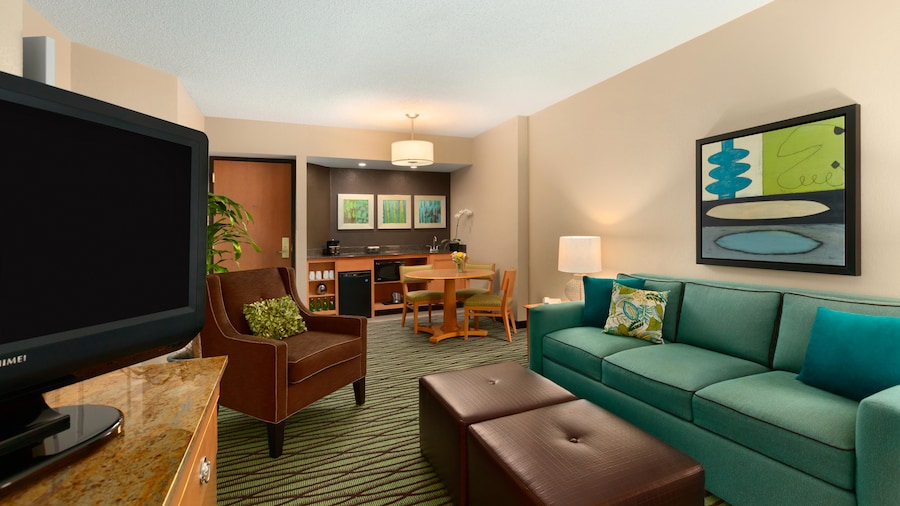 Una habitación con sofá, sillas, TV, comedor, cocineta y obras de arte en las paredes